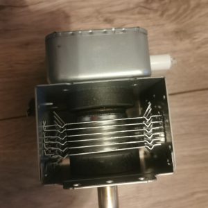 Close-up of an electric appliance component: a metal motor housing with a rectangular frame holding parallel metal wires inside. A cylindrical shaft extends from the bottom.
