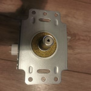 Close-up of a silver door lock mechanism with a brass circular housing and central spindle, mounted on a rectangular metal plate viewed from above.