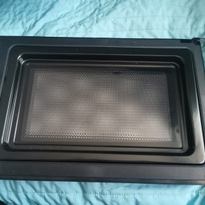 Open oven cavity with a perforated metal baking tray inside a black frame on a teal surface (informative).]}{