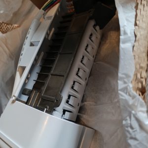 Close-up of an electronic control module with a black vented housing and white plastic casing, showing multicolored wires exposed.