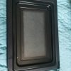 Rectangular black vent panel with a perforated metal screen and mounting clips at the top.
