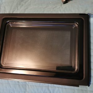 Disassembled oven door with inner metal frame and perforated panel on a blue quilt backdrop