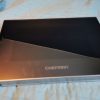 Open Chefman box with black interior on a blue quilted bedspread, lid raised to show empty cavity.