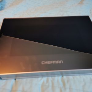 Open Chefman box with black interior on a blue quilted bedspread, lid raised to show empty cavity.