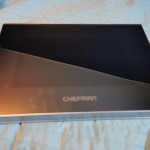 Opened CHEFMAN box with a black interior resting on a blue quilted bedspread around the edges visible.