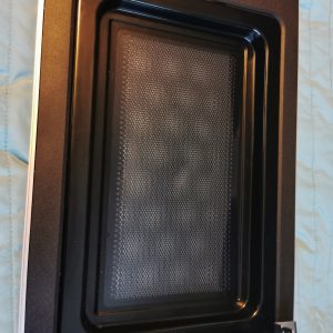 Close-up of a black oven interior with a perforated baking tray inside.