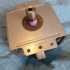 Close-up of a metal square actuator housing with a central cylindrical shaft and pink seal around it.