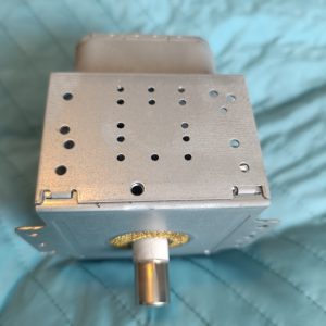 Metal rectangular electronic component with a perforated top and a cylindrical shaft protruding from the bottom, placed on a blue quilted surface.
