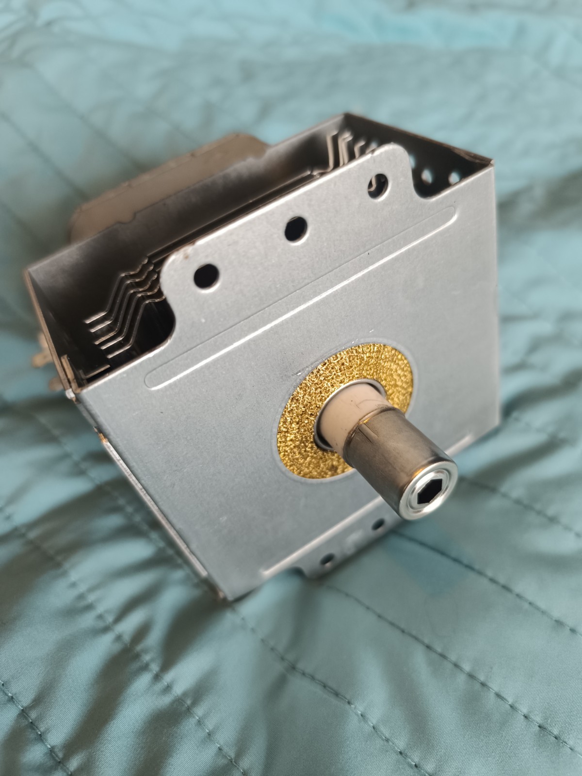 s-l1600-792.jpg Close-up of a small metal mechanical assembly with a hollow shaft and a gold washer, showing a stack of leaf springs and vent holes in the casing.