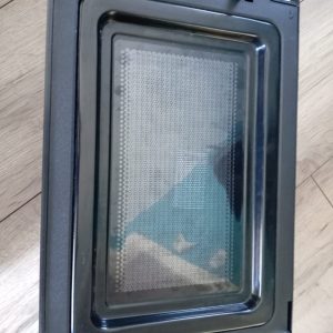 Black oven door with a glass viewing window, lying on a wooden floor; inner metal frame and gasket are visible.