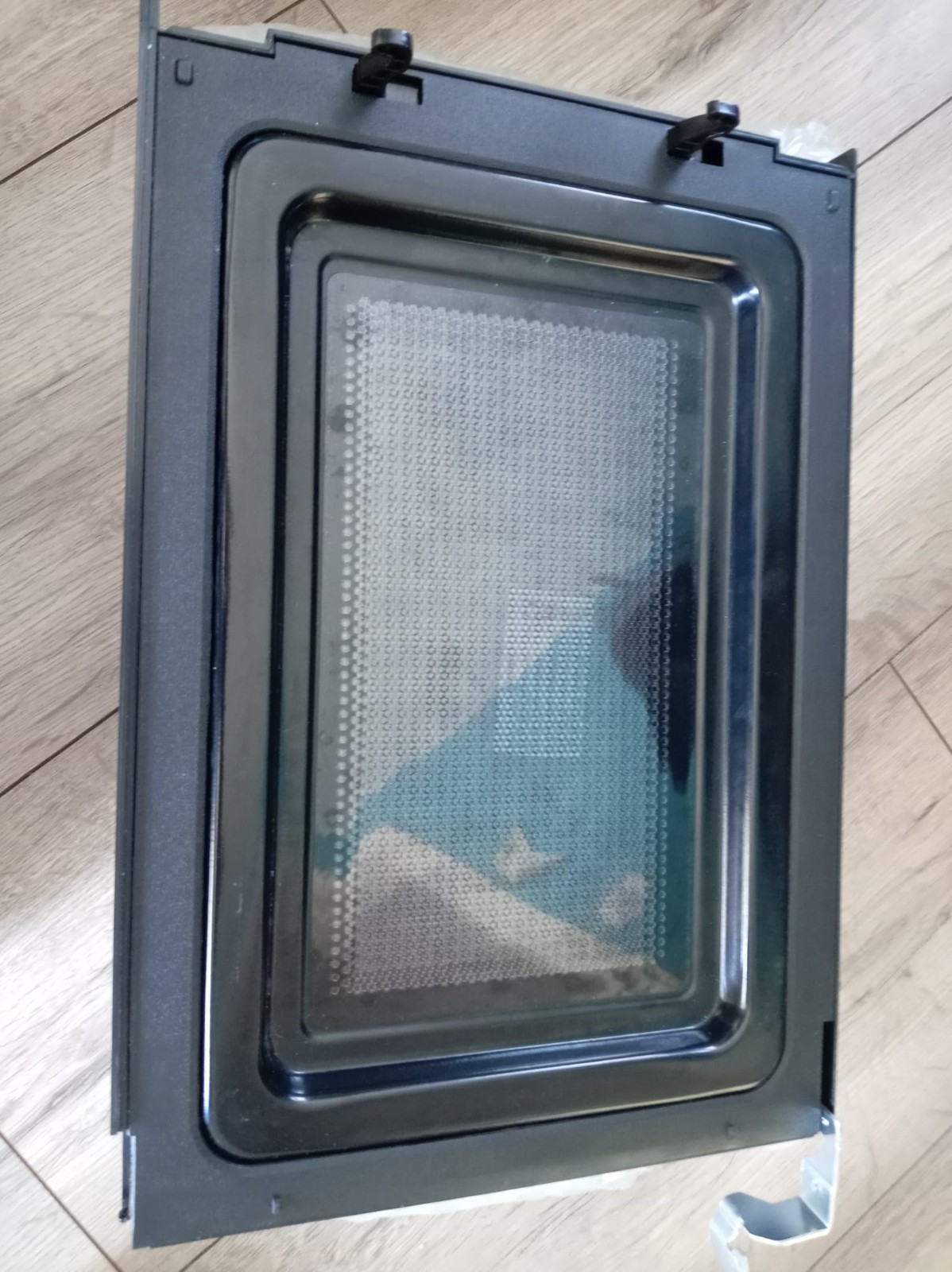 s-l1600-856.jpg Black oven door with a glass viewing window, lying on a wooden floor; inner metal frame and gasket are visible.