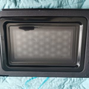 Black oven/microwave door with a perforated inner panel laid on a teal quilted surface.