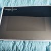 Closed laptop with a glossy black lid showing the Russell Hobbs logo on a white frame, placed on a blue quilted surface.