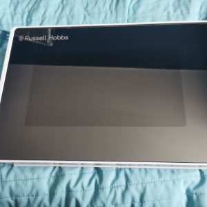 Closed laptop with a glossy black lid showing the Russell Hobbs logo on a white frame, placed on a blue quilted surface.