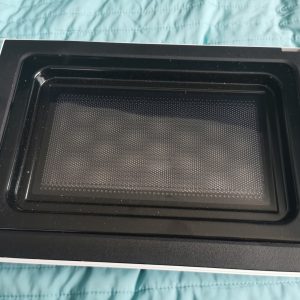 Inside view of a black toaster/oven with a metal baking tray and perforated bottom resting inside, placed on a teal quilted surface.