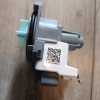 Close-up of a gray plastic mechanical component with a white label showing a QR code and serial number, placed on wood floor.