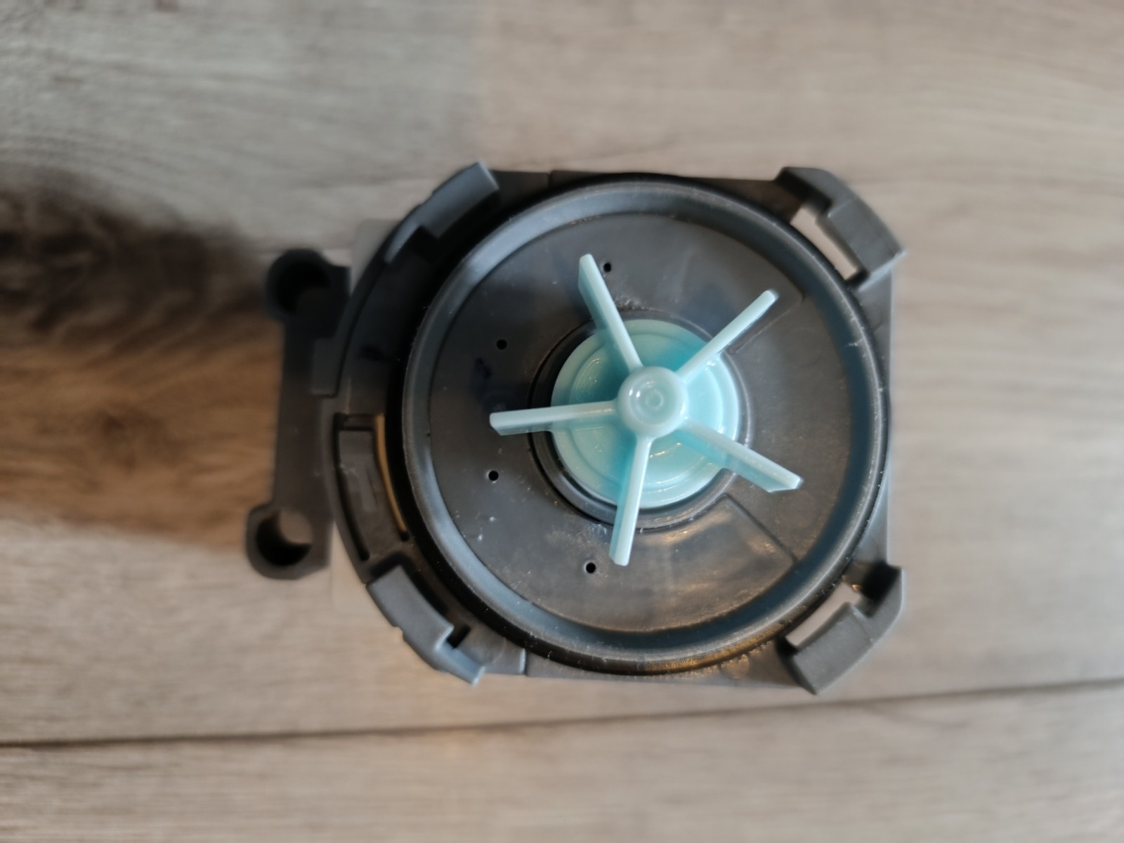 s-l1600-910.jpg Close-up of a gray circular plastic component with a light blue four-spoke impeller in the center on a wooden surface.