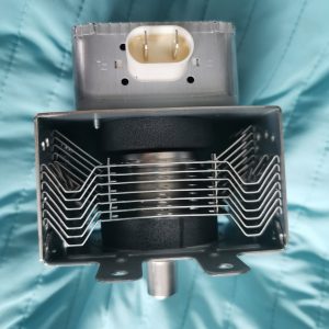 Close-up of an electric deep fryer interior with a metal wire basket and a white plastic connector on the top against a teal background.