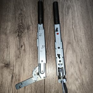 Two long metal mechanical components with black coiled springs on top, lying on a wooden floor; likely parts of a hinge/door mechanism with a red indicator on one piece